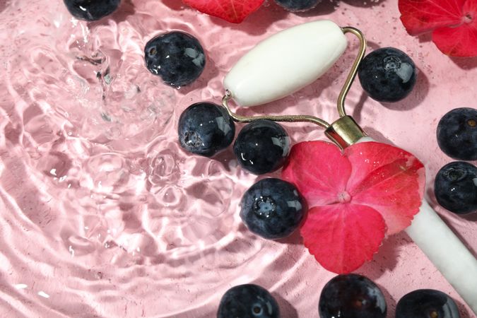 Top view of blueberries and flowers soaking in water with face roller