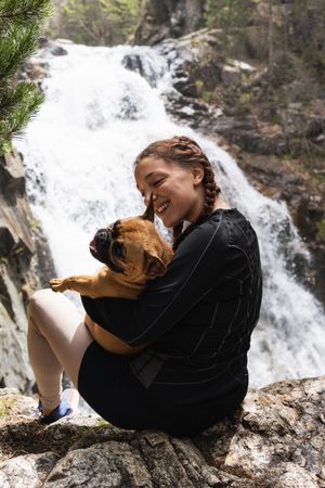 Cheerful traveling woman with dog near waterfall in forest