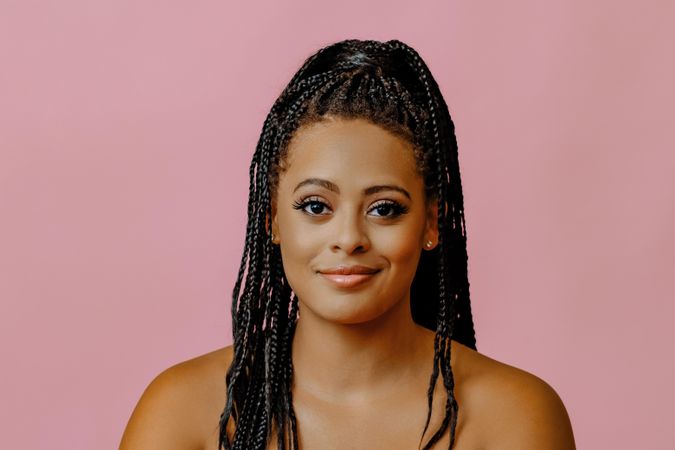 Smiling Black woman with braided hair looking at camera in pink studio shoot