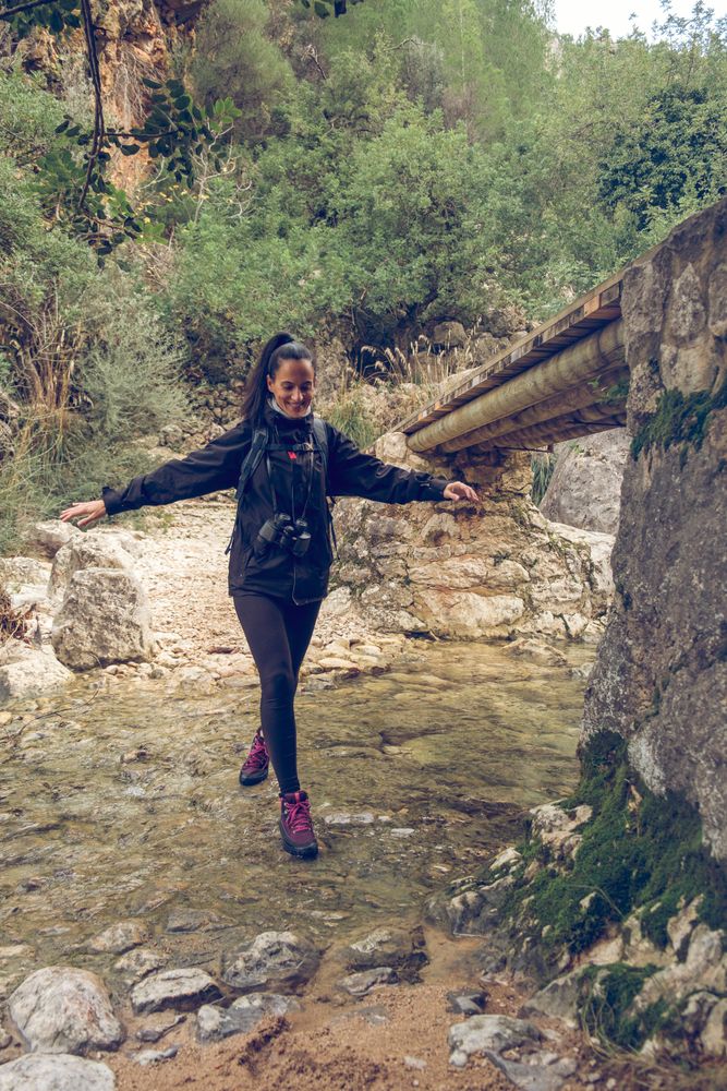Happy woman crossing shallow river while hiking in rocky terrain