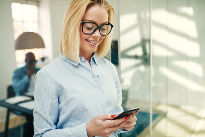 Portrait of blonde businesswoman smiling and checking her cell phone