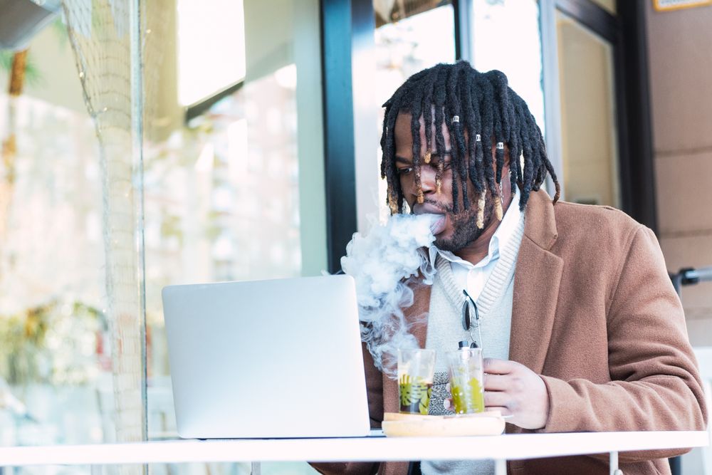 Smoking Black man using laptop on restaurant terrace