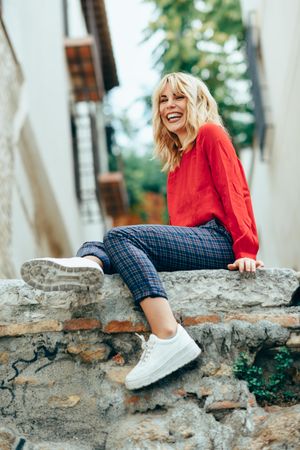 Smiling blond woman sitting on stone wall