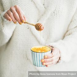 Woman in sweater adding raw honey to latte cup 0vawdb
