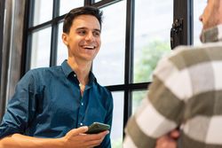 Male employee in shirt holding smartphone speaking with co worker
