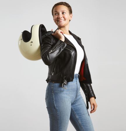 Smiling woman in dark leather jacket with light t-shirt posing with motorcycle helmet over shoulder