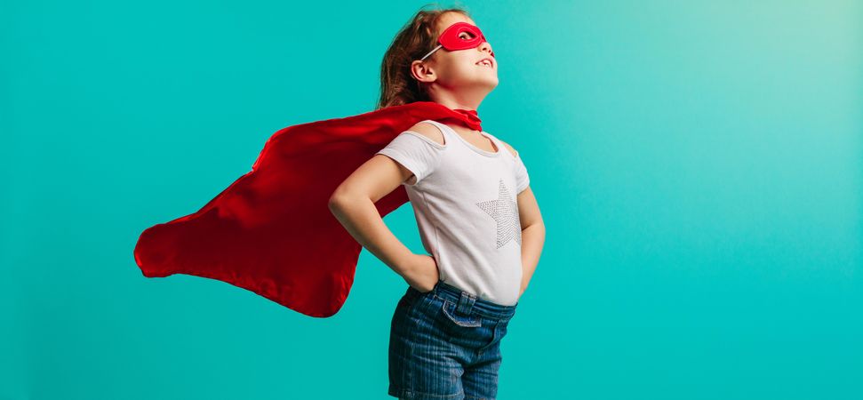 Girl child wearing red superhero costume standing with her hands on hips in studio