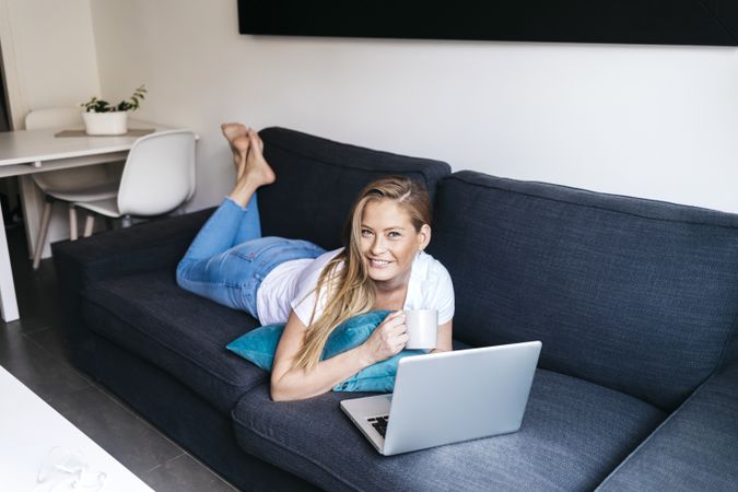 Pretty long haired female lying on sofa with laptop computer