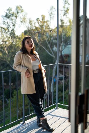 Young woman in cute outfit leaning on patio railing with view behind