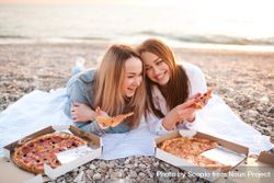 Two smiling women eating pizza on seashore 4Mkqr0