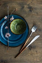 Top view of table setting with small bowl on ceramic navy plate and delicate cherry blossom branch