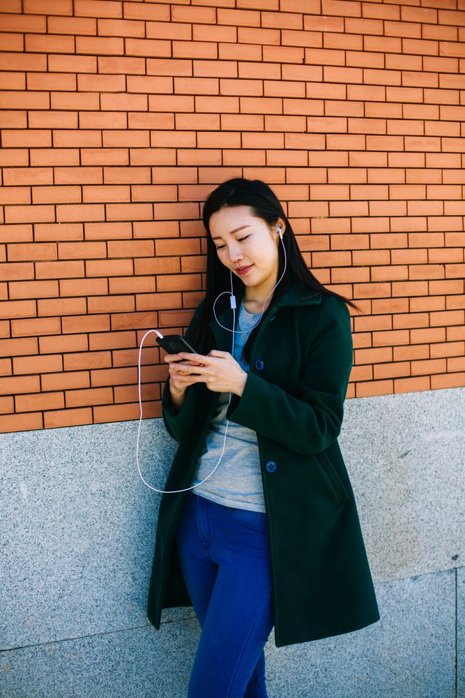 Asian female listening to music near brick wall