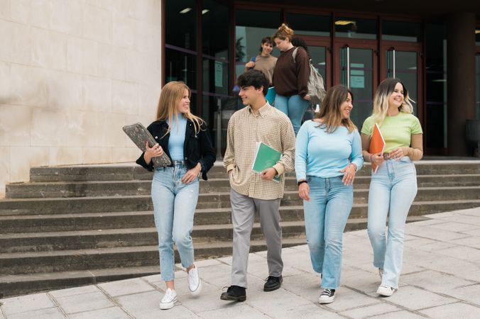 Happy young friends walking near university building after studies