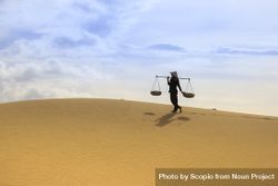 Rice farmer wearing conical hat and holding carrying pole in desert 0gok70