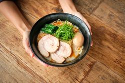 Crop woman showing bowl of traditional Japanese noodle dish