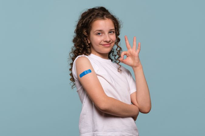 Smiling girl making an "OK" gesture after vaccinated