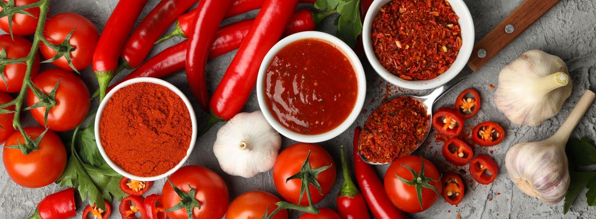 Composition with chilli pepper, powder spice, garlic and sauce on gray background