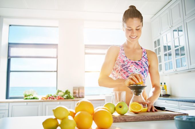 Muscular woman juicing an orange in her bright kitchen