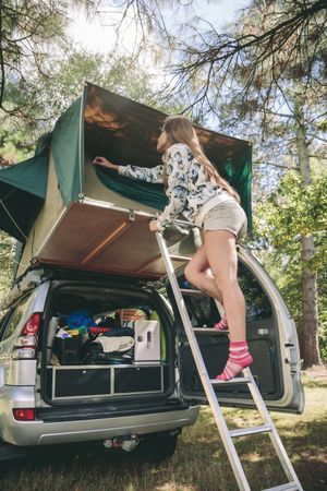 Woman standing in ladder closing tent above car