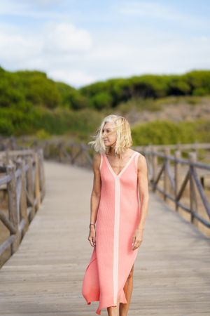 Older woman with grey hair strolling on wooden walkway near the coast, vertical