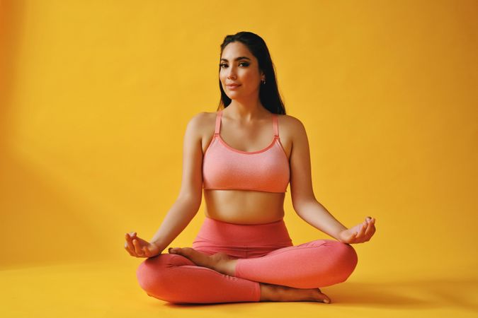 Hispanic female sitting in meditative yoga pose in yellow studio shoot