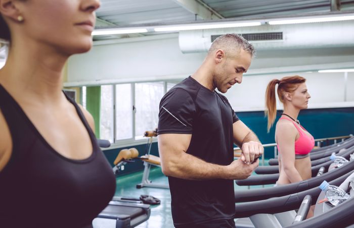 Man checking watch on treadmill in busy gym