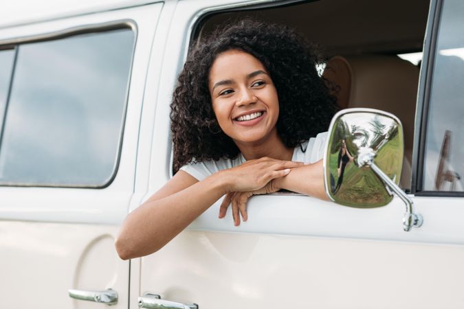 Happy woman with curly hair leaning out of a car window