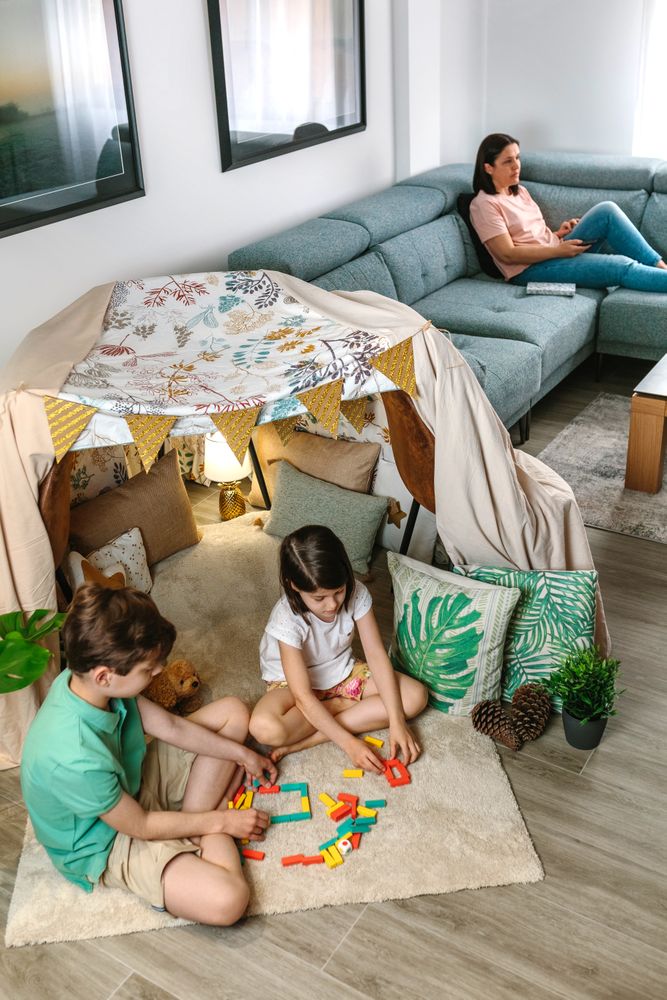 Children playing with stacking piece game while relaxed mother using remote control sitting on sofa