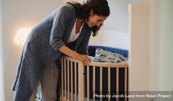 Woman looking at her baby in crib and smiling down at him 5z2Kj5