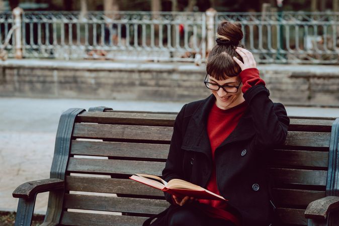 Young woman reading book on bench in park