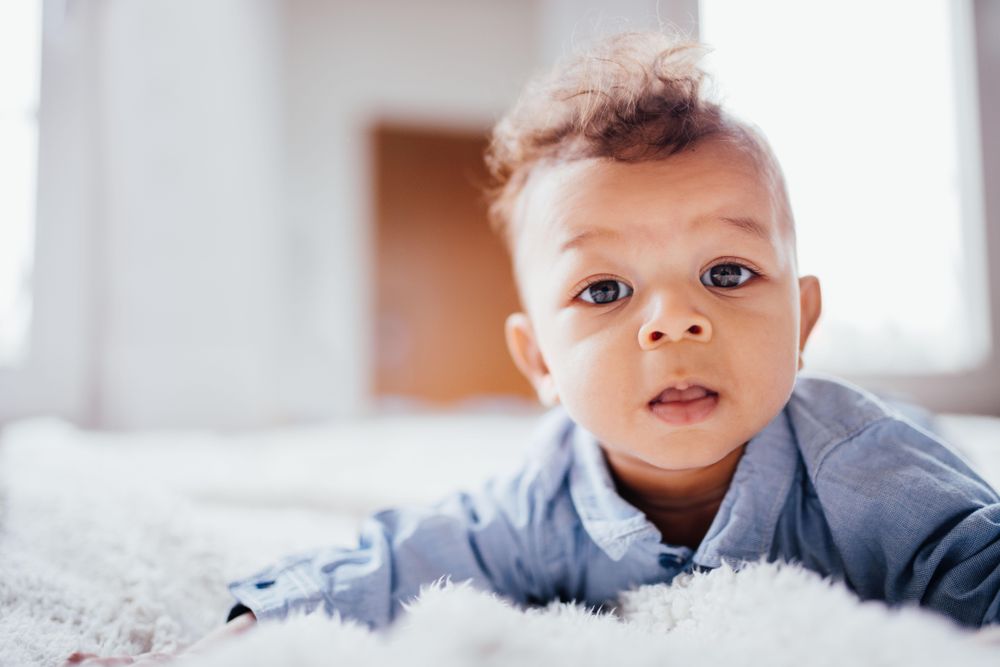 Baby boy lying on his belly looking with wonder into the camera