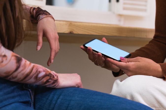 Unrecognizable women using smartphone together in bar