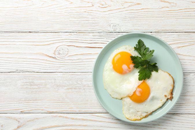 Top view of two eggs sunny side up on blue plate, copy space