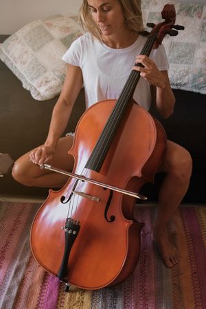 Crop woman playing cello at home
