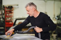 Mechanic grinding paint from car detail
