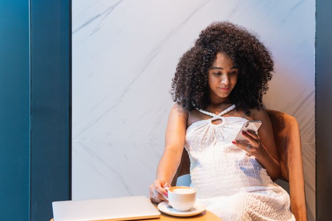 Black woman browsing on smartphone with cup of latte