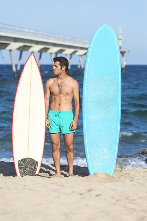 Shirtless male surfer standing with two boards on the coast