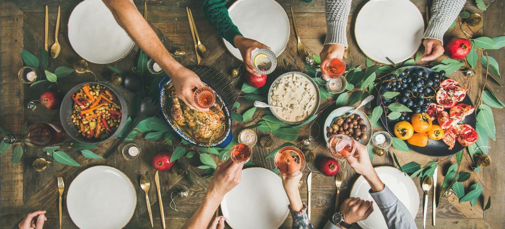 Group toasting at festive table with roasted chicken and pomegranates, wide composition