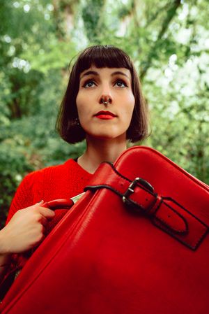 Woman in red with big red suitcase in forest