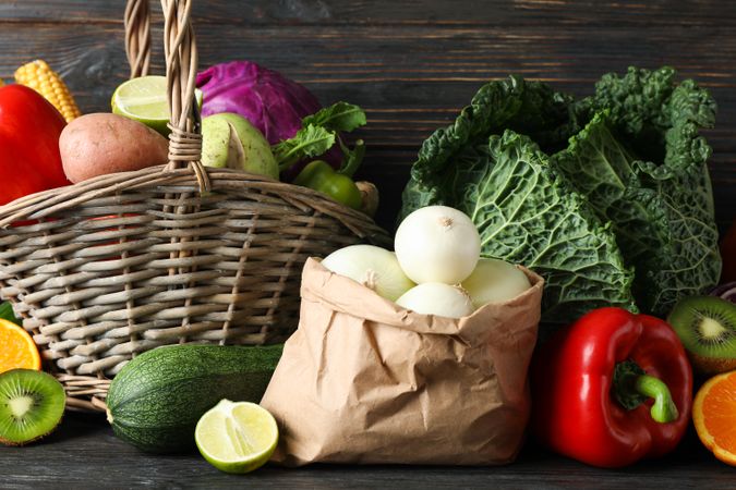 Vegetables, fruits, wicker basket and paper bag on wood background, copy space