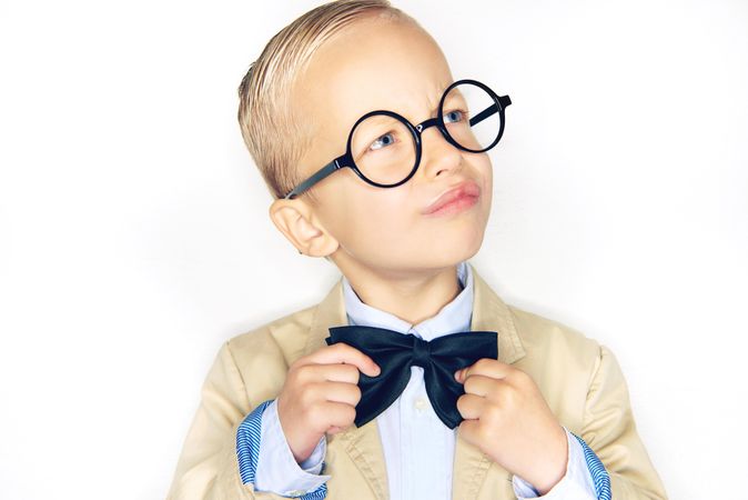 Blond boy making an inquisitive face wearing round glasses and bow tie