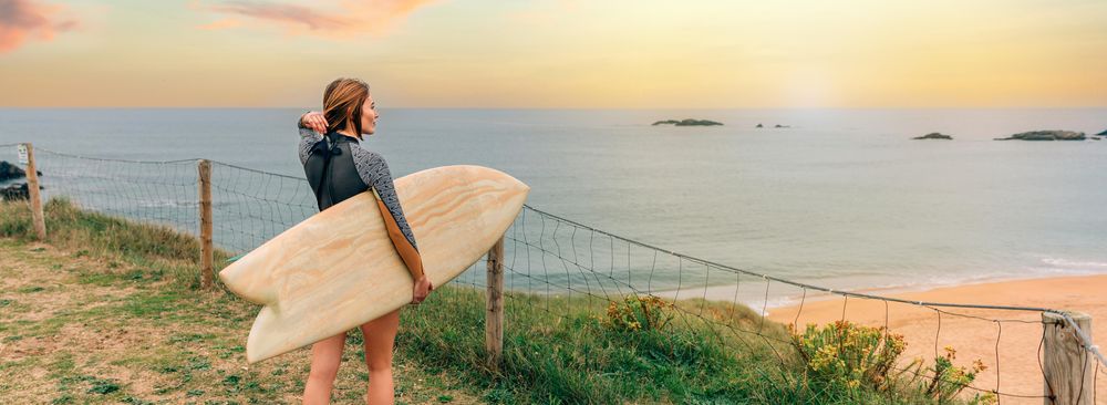 Female walking with surfboard atop of cliff with beautiful coastal view, banner