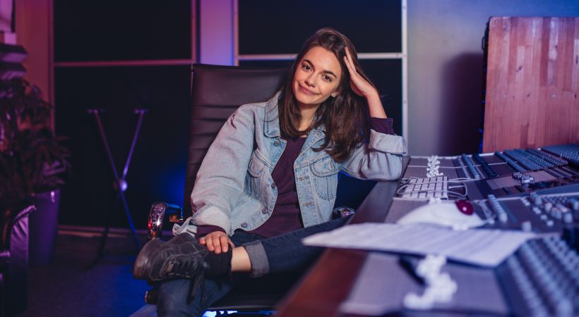 Confident female  sitting by audio mixing console in sound recording studio