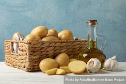 Side view of potatoes, olive oil and garlic next to wicker basket 4AQEN4