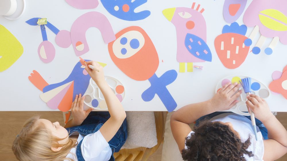 Top view of two young children making shapes with colorful cartoon papers