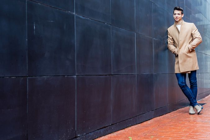 Man in fall coat leaning against dark wall outside