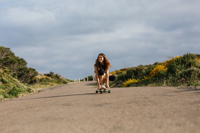 Smiling woman riding longboard on asphalt road