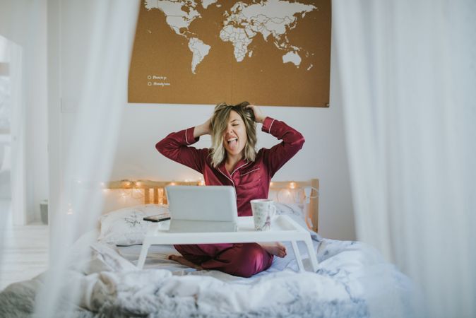 Woman stretching in bed with laptop