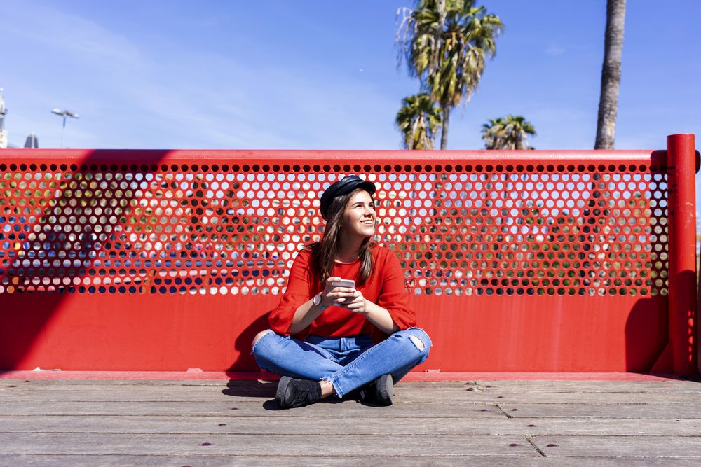 Woman in red sitting cross legged using a mobile phone outdoors on a bright day