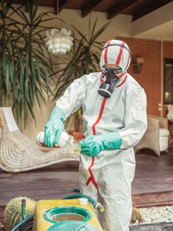 Man in suit for fumigation pouring chemical into tank